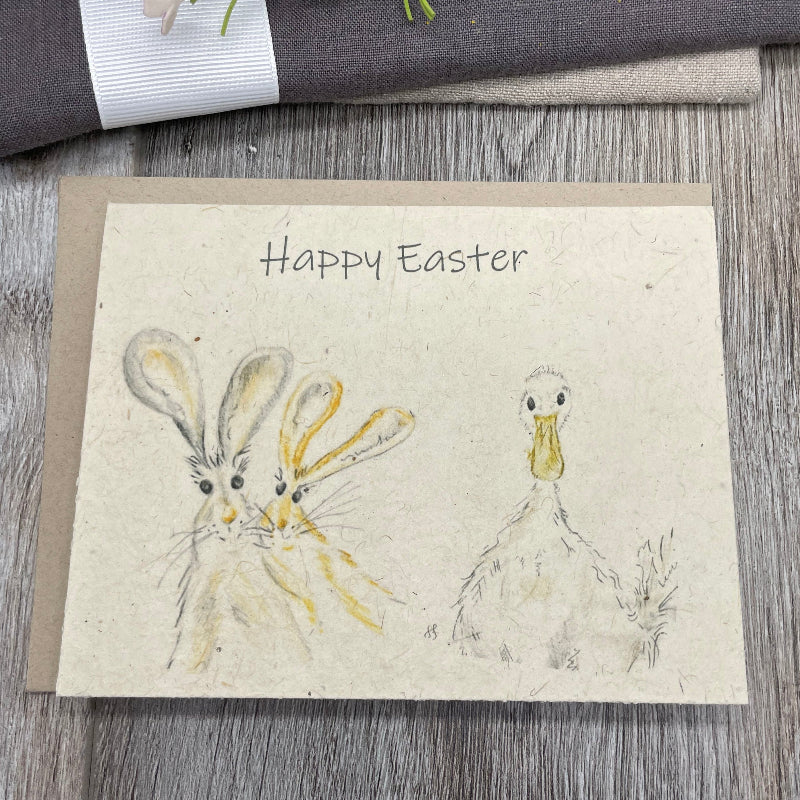 A folded plantable card with 'Happy Easter' written at the top and illustrations of a rabbit and a duck on the front. The card is made of wildflower seed paper. bunnies, easter. childrens duck