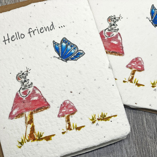 mouse on a red poka dot mushroom looking at a blue butterfly. Greeting card made from wildflower seed paper.  Grows wildflowers by 1 simple seed.