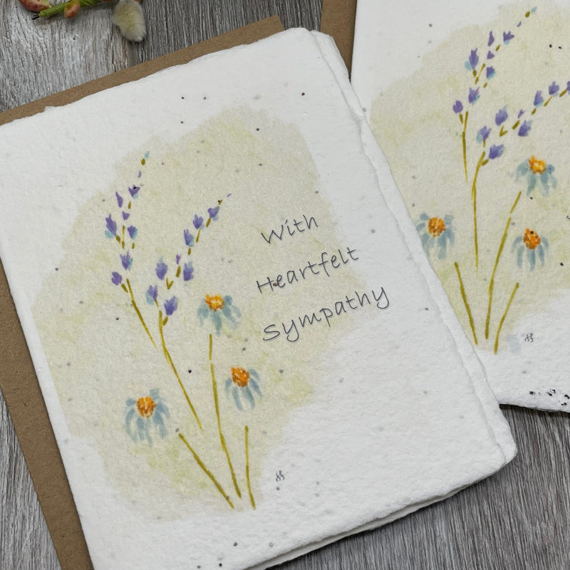 A handmade sympathy card made from textured cream paper with a brown kraft envelope, decorated with watercolor purple wildflowers and the handwritten message 'With Heartfelt Sympathy'.